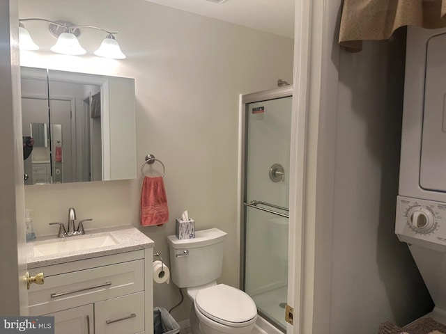 bathroom featuring a shower with door, toilet, vanity, and stacked washing maching and dryer