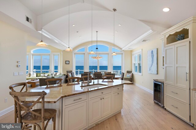 kitchen featuring pendant lighting, sink, a kitchen island with sink, a water view, and wine cooler