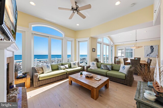 living room with a fireplace, light hardwood / wood-style floors, ceiling fan, and a water view