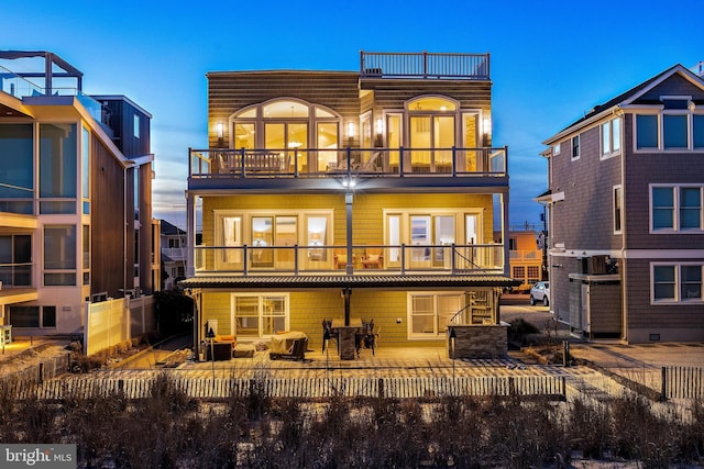 back house at dusk featuring a patio and a balcony