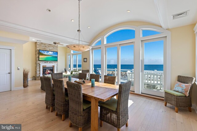 dining area with a stone fireplace, vaulted ceiling, and light wood-type flooring