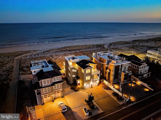 aerial view at dusk featuring a water view and a beach view