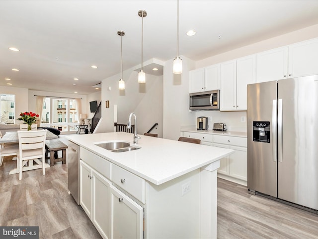 kitchen featuring an island with sink, appliances with stainless steel finishes, pendant lighting, white cabinets, and sink