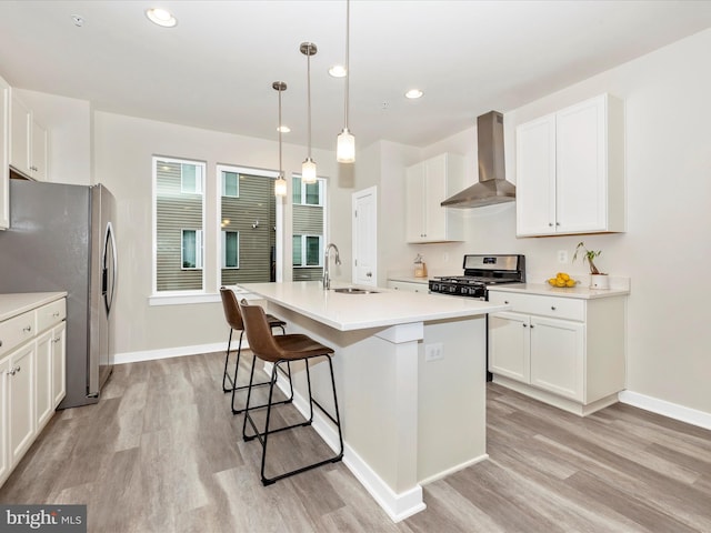 kitchen with decorative light fixtures, wall chimney range hood, stainless steel appliances, sink, and a center island with sink