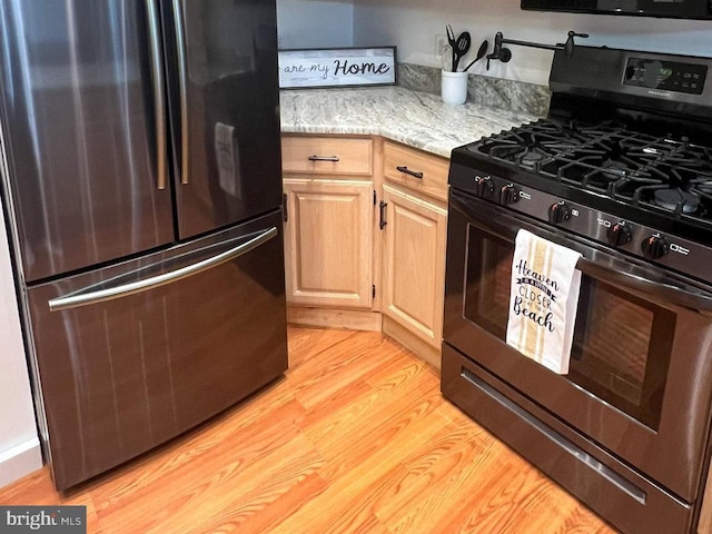 kitchen with gas range, stainless steel refrigerator, light hardwood / wood-style flooring, light brown cabinets, and light stone counters