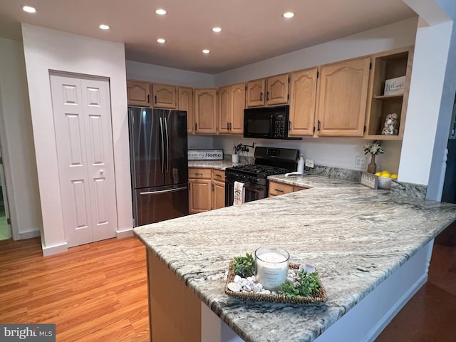 kitchen with black appliances, light brown cabinetry, kitchen peninsula, light wood-type flooring, and light stone counters