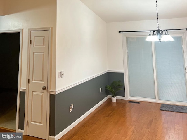 unfurnished dining area with an inviting chandelier and hardwood / wood-style floors