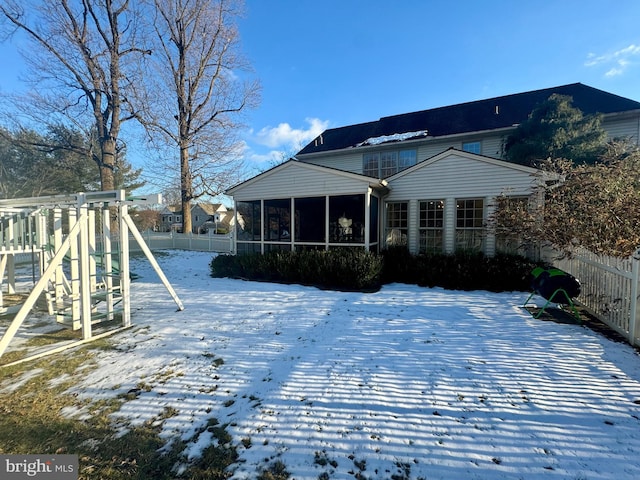 snow covered house with a playground and a sunroom