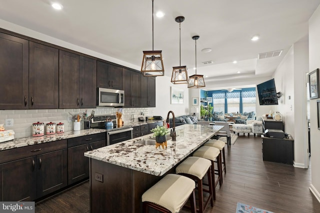 kitchen featuring decorative light fixtures, sink, dark brown cabinetry, a kitchen island with sink, and stainless steel appliances