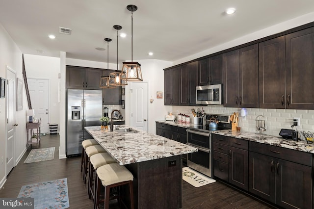 kitchen featuring light stone countertops, decorative light fixtures, stainless steel appliances, an island with sink, and sink