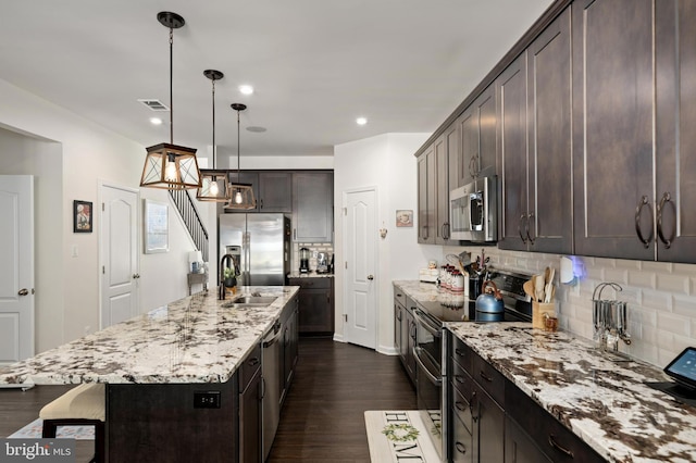 kitchen with pendant lighting, appliances with stainless steel finishes, an island with sink, decorative backsplash, and sink