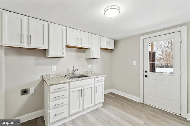 kitchen featuring white cabinetry, sink, light stone counters, and light hardwood / wood-style flooring