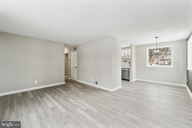 unfurnished living room featuring a textured ceiling, a notable chandelier, and light wood-type flooring