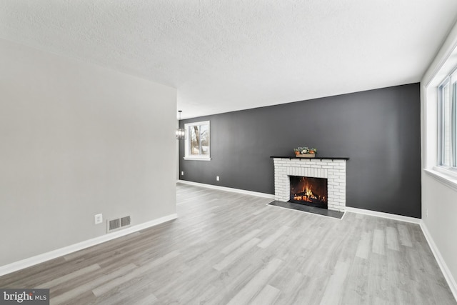 unfurnished living room with a brick fireplace, an inviting chandelier, a textured ceiling, and light wood-type flooring