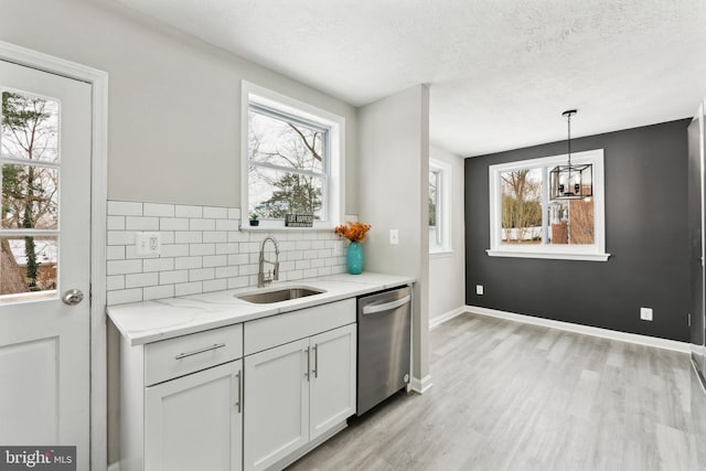 kitchen featuring sink, white cabinetry, hanging light fixtures, light stone countertops, and stainless steel dishwasher