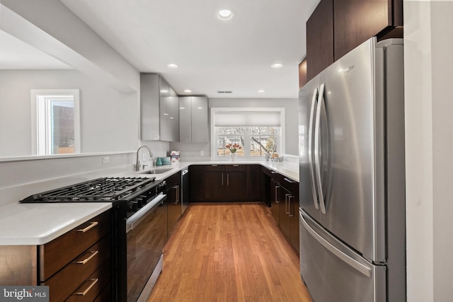 kitchen with modern cabinets, light countertops, light wood-type flooring, black appliances, and a sink