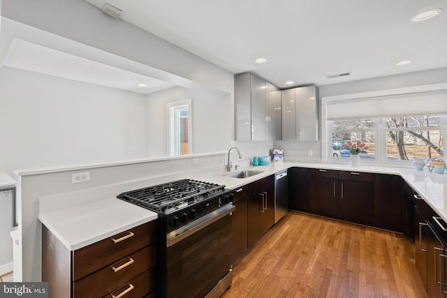 kitchen with visible vents, gas range oven, light countertops, light wood-style floors, and a sink