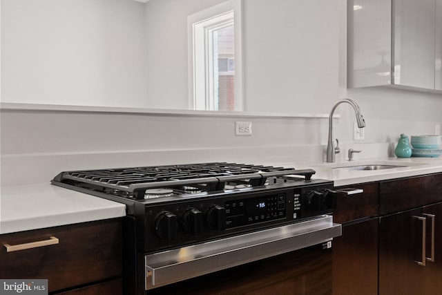 kitchen featuring range with gas stovetop, light countertops, white cabinets, a sink, and dark brown cabinets