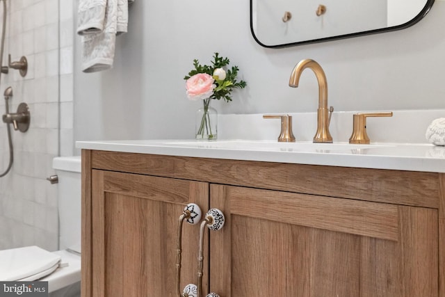 bathroom with toilet, tiled shower, and vanity