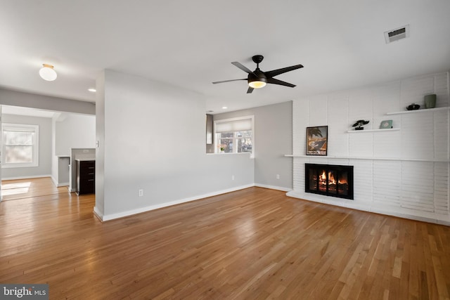 unfurnished living room with a brick fireplace, visible vents, light wood-style flooring, and baseboards