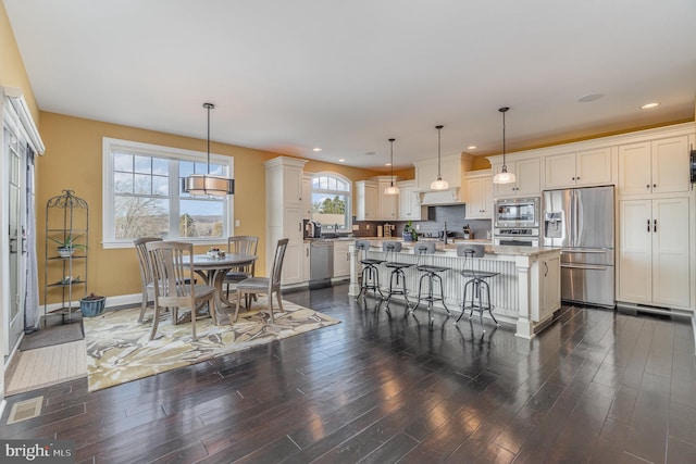 kitchen with a center island, a breakfast bar, white cabinetry, hanging light fixtures, and appliances with stainless steel finishes