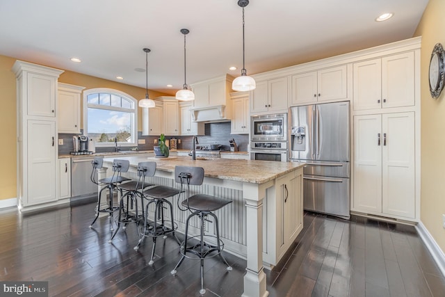 kitchen with pendant lighting, appliances with stainless steel finishes, decorative backsplash, a kitchen island with sink, and light stone counters