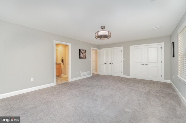 unfurnished bedroom featuring carpet, two closets, and ensuite bath