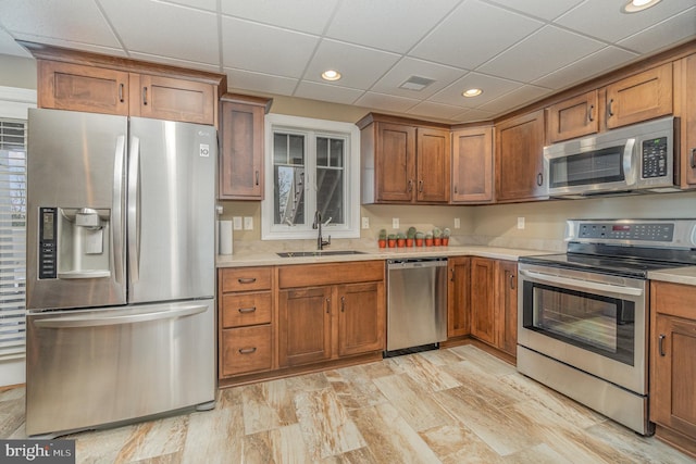 kitchen featuring light wood-type flooring, stainless steel appliances, a drop ceiling, and sink