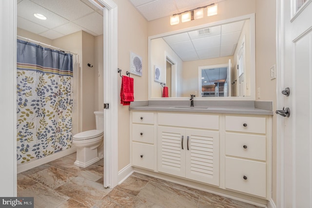 bathroom featuring toilet, a paneled ceiling, walk in shower, and vanity