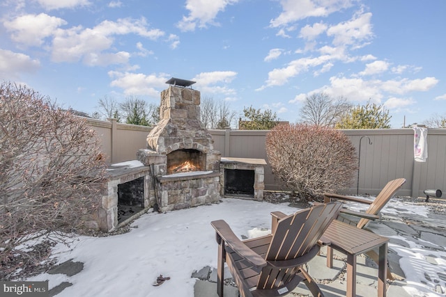 snow covered patio with an outdoor stone fireplace