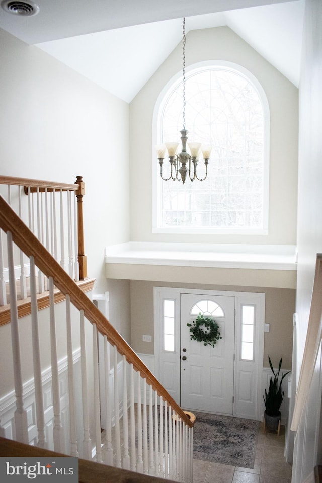 tiled foyer with lofted ceiling, a healthy amount of sunlight, and an inviting chandelier