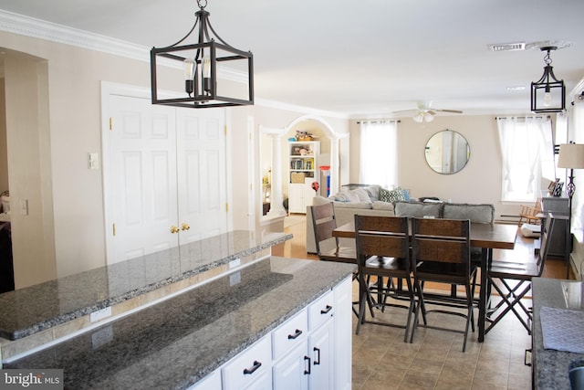 kitchen featuring dark stone counters, a wealth of natural light, pendant lighting, ceiling fan with notable chandelier, and white cabinets