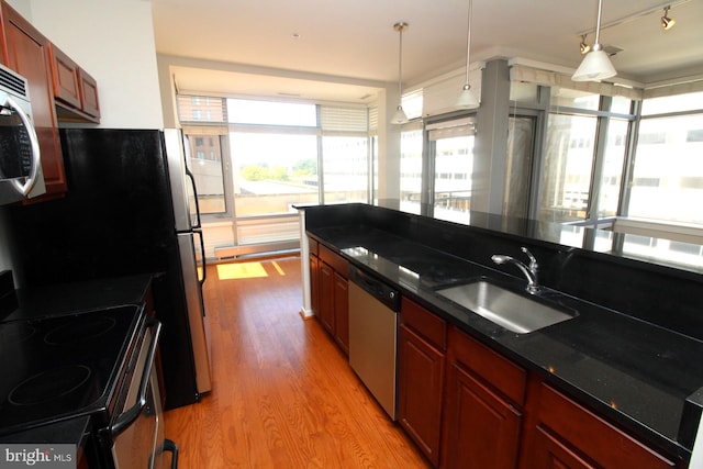 kitchen featuring stainless steel appliances, decorative light fixtures, dark stone countertops, light hardwood / wood-style flooring, and sink