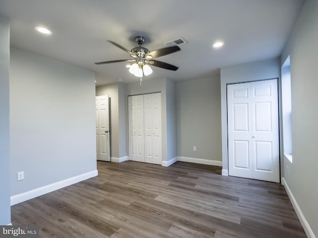 unfurnished bedroom with ceiling fan, dark hardwood / wood-style floors, and two closets