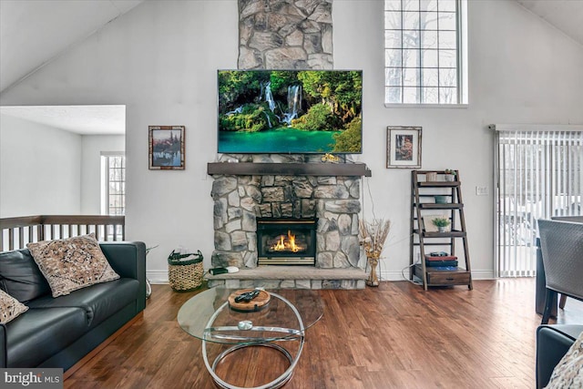 living room featuring a high ceiling, wood-type flooring, and a stone fireplace