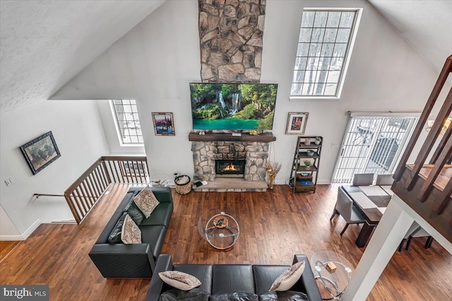 living room with a healthy amount of sunlight, wood-type flooring, a fireplace, and a towering ceiling