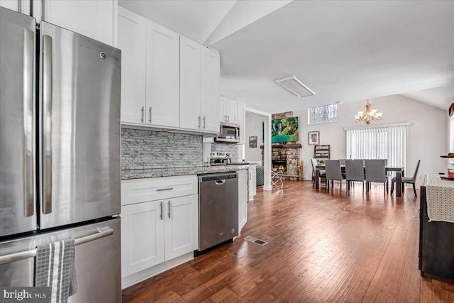 kitchen with decorative light fixtures, white cabinetry, stainless steel appliances, decorative backsplash, and light stone counters