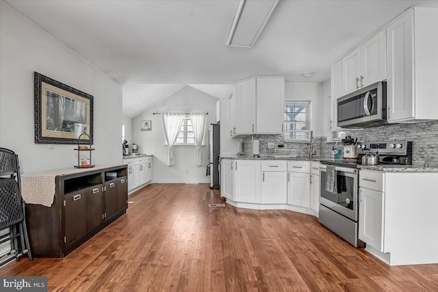 kitchen with appliances with stainless steel finishes, lofted ceiling, wood-type flooring, white cabinetry, and tasteful backsplash