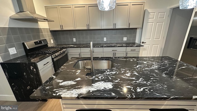 kitchen with gas range, sink, wall chimney exhaust hood, and dark stone counters