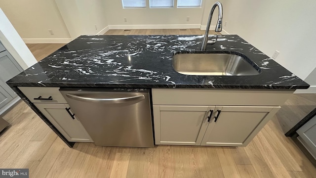 kitchen with stainless steel dishwasher, sink, dark stone countertops, and a center island with sink