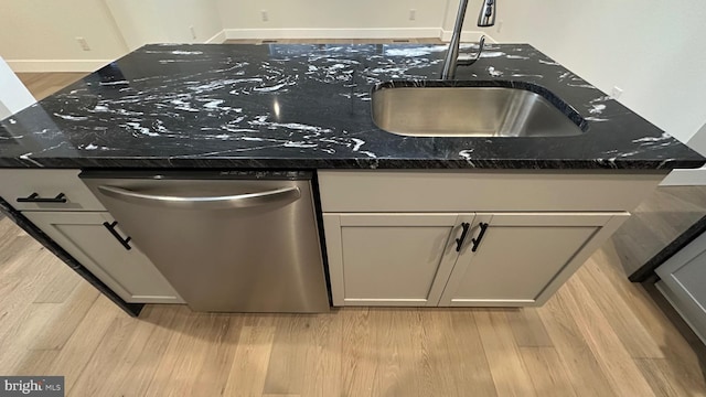 kitchen with light wood-type flooring, dark stone countertops, dishwasher, and sink