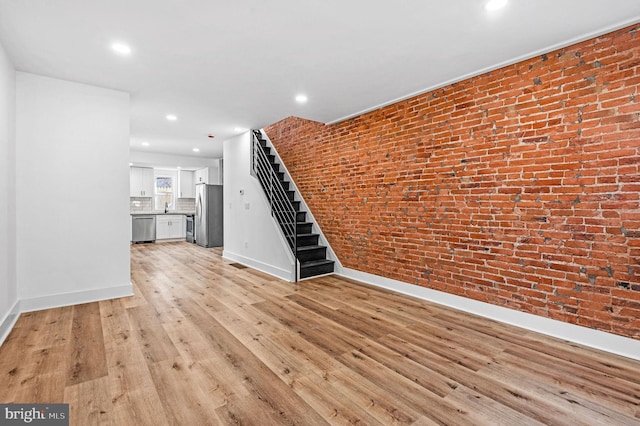 unfurnished living room with light hardwood / wood-style floors and brick wall