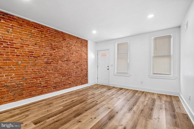 unfurnished room with brick wall and light hardwood / wood-style floors