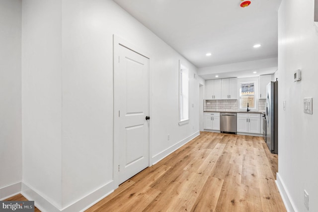 kitchen featuring stainless steel appliances, decorative backsplash, white cabinets, light hardwood / wood-style flooring, and sink