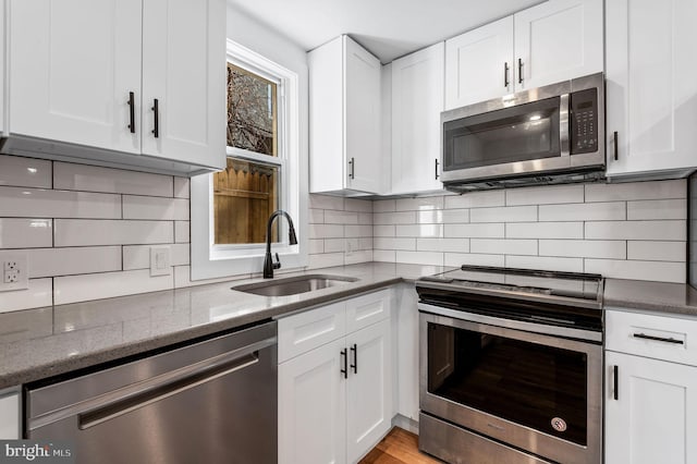 kitchen featuring appliances with stainless steel finishes, white cabinetry, dark stone counters, decorative backsplash, and sink