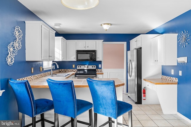 kitchen with sink, white cabinets, light tile patterned floors, kitchen peninsula, and stainless steel appliances