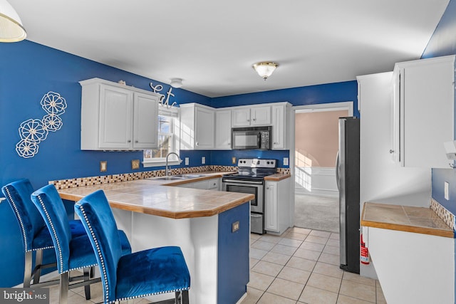 kitchen with appliances with stainless steel finishes, tile countertops, white cabinetry, sink, and kitchen peninsula