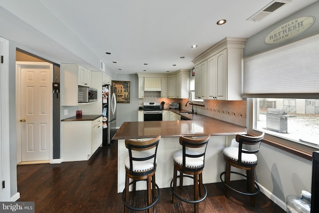 kitchen with sink, a breakfast bar area, appliances with stainless steel finishes, dark hardwood / wood-style flooring, and kitchen peninsula