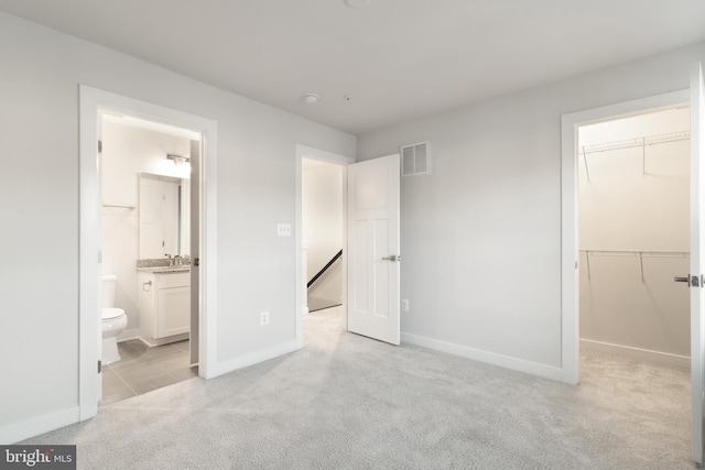 unfurnished bedroom featuring a closet, a walk in closet, connected bathroom, and light colored carpet