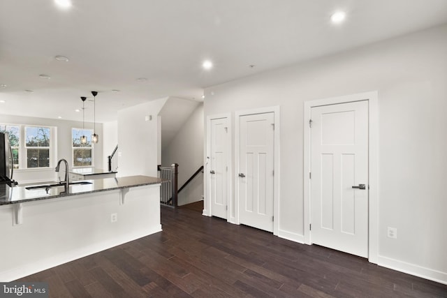 kitchen with dark hardwood / wood-style floors, pendant lighting, a kitchen bar, sink, and dark stone counters